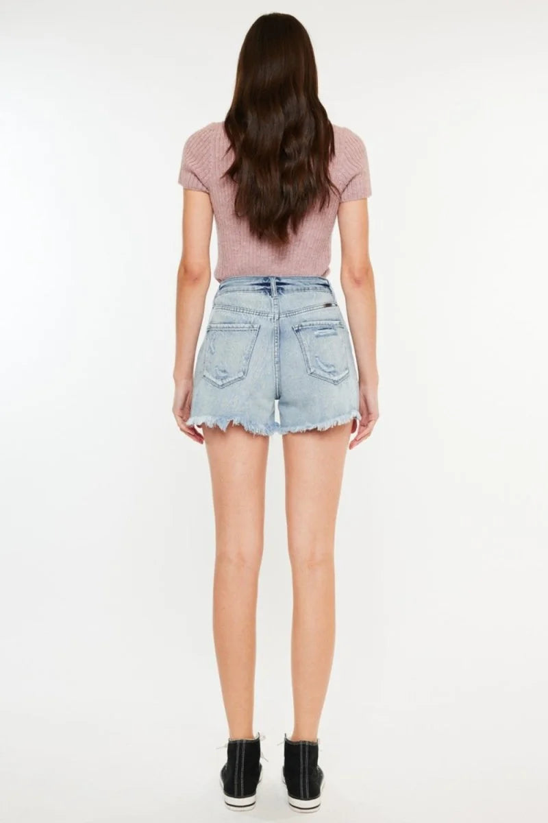 Light wash distressed denim shorts with frayed hem, shown from the back on a model.