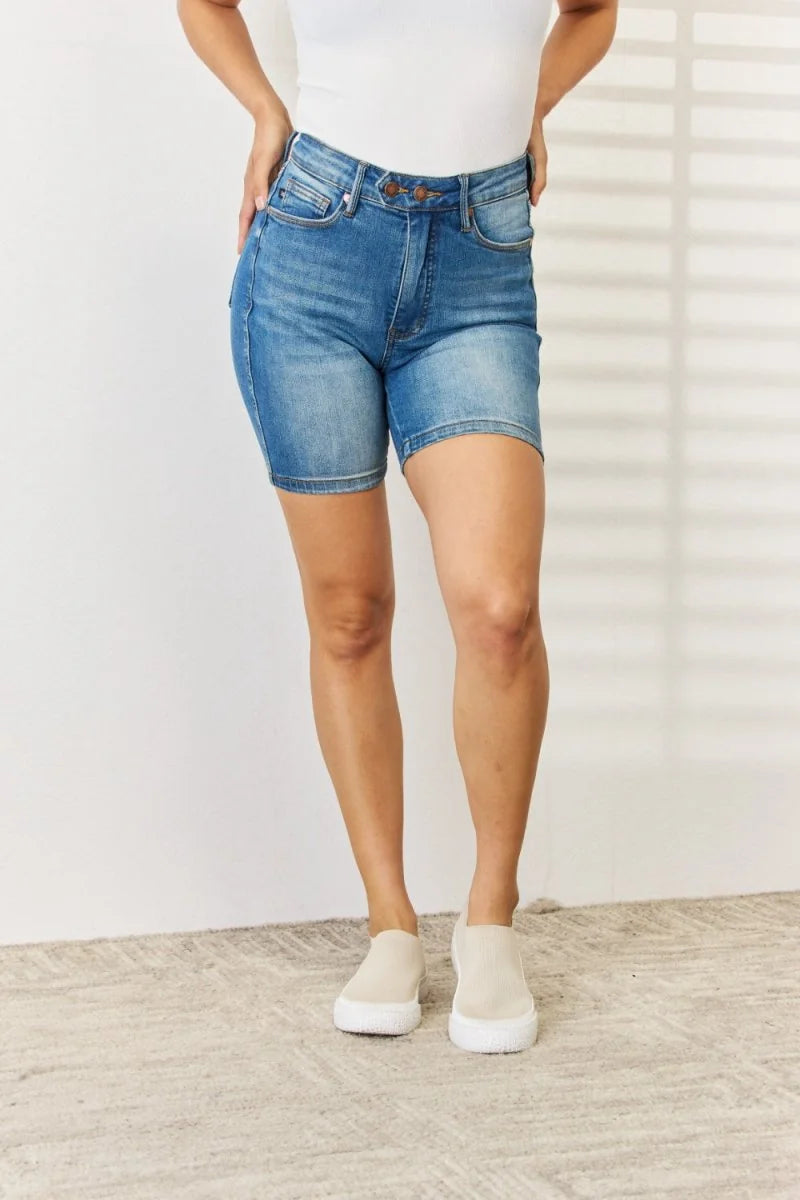 Blue denim shorts on a model, featuring a mid-rise waist and a slim fit, made of cotton, polyester, and spandex blend.