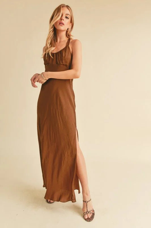 A woman wears a flowing, brown satin maxi dress with a thigh-high slit and leopard print sandals.