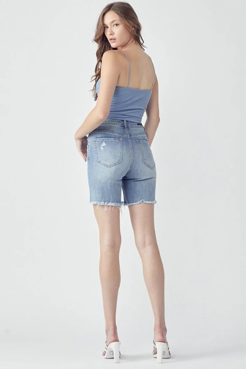 Distressed light wash denim bermuda shorts with frayed hem, shown from the back on a model.