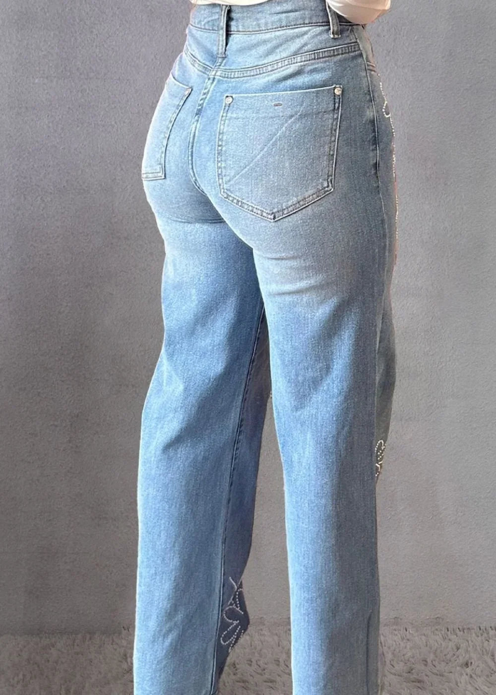 Light wash denim jeans with rhinestone embellishments on the leg, shown from the back.
