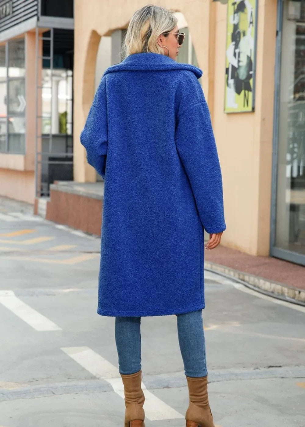 Back view of a cobalt blue textured teddy coat with a wide collar, worn over blue jeans and tan boots.