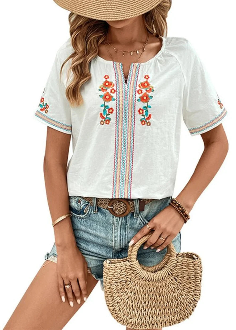 White embroidered top with floral details and denim shorts on a model.