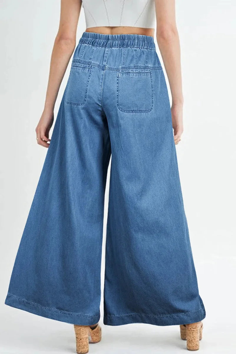Back view of light wash denim palazzo pants with elastic waistband and patch pockets.