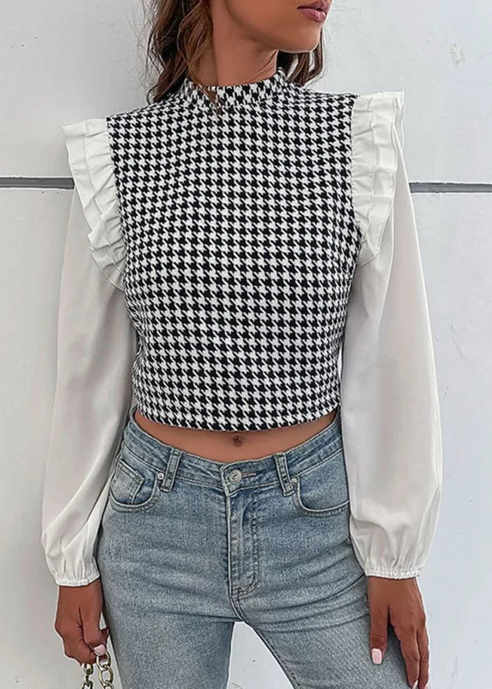 Woman wearing a black and white houndstooth crop top with ruffled sleeves and light wash jeans.
