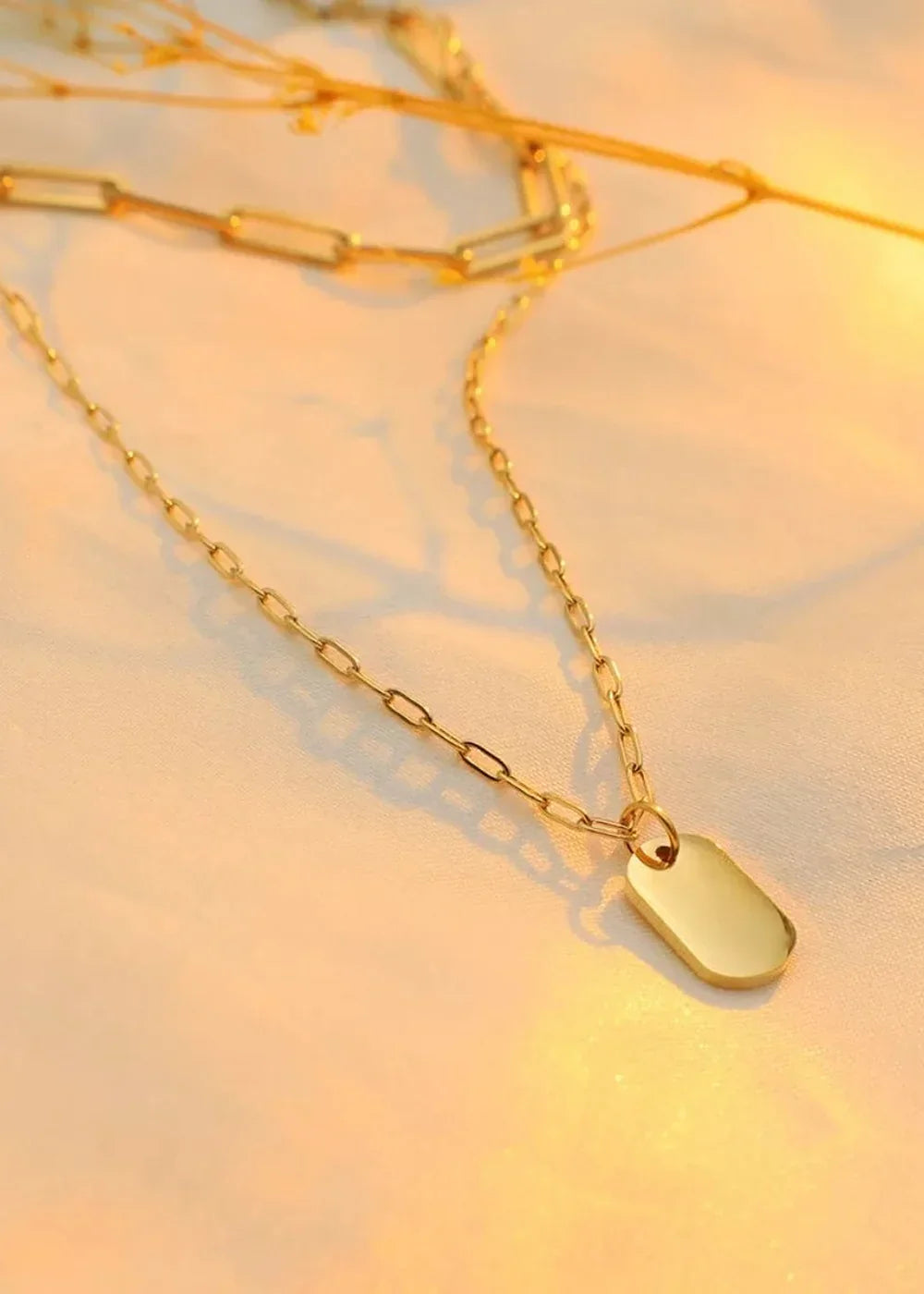 Gold chain necklace with a smooth, elongated oval pendant, on a white satin surface with warm lighting.