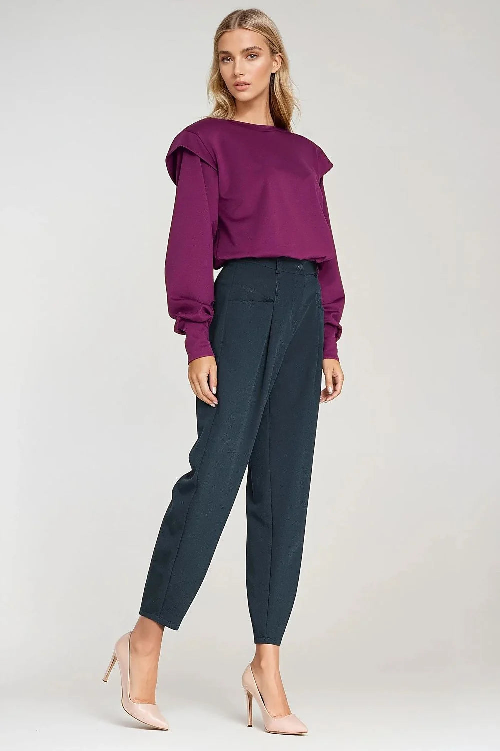 Woman in a plum sweatshirt with shoulder pads and dark teal pants with pointed nude heels.