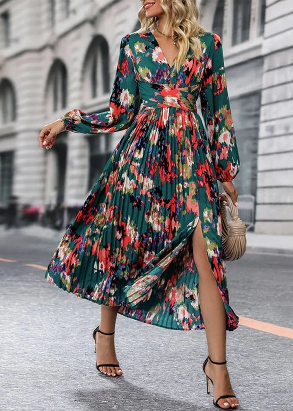 A woman in a green floral print midi dress with a v-neck, long sleeves, and a high slit, holding a woven bag.