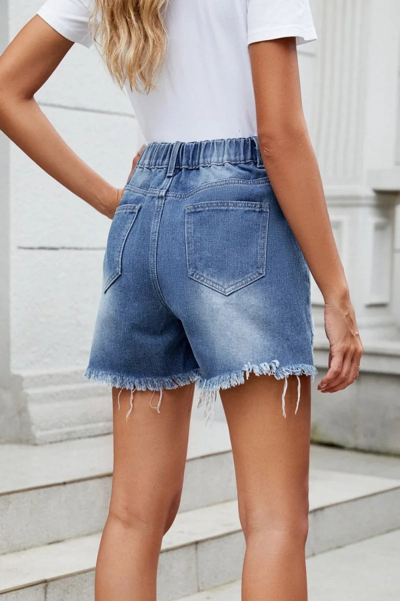 Distressed denim shorts with frayed hem and elastic waistband, shown from the back on a model.