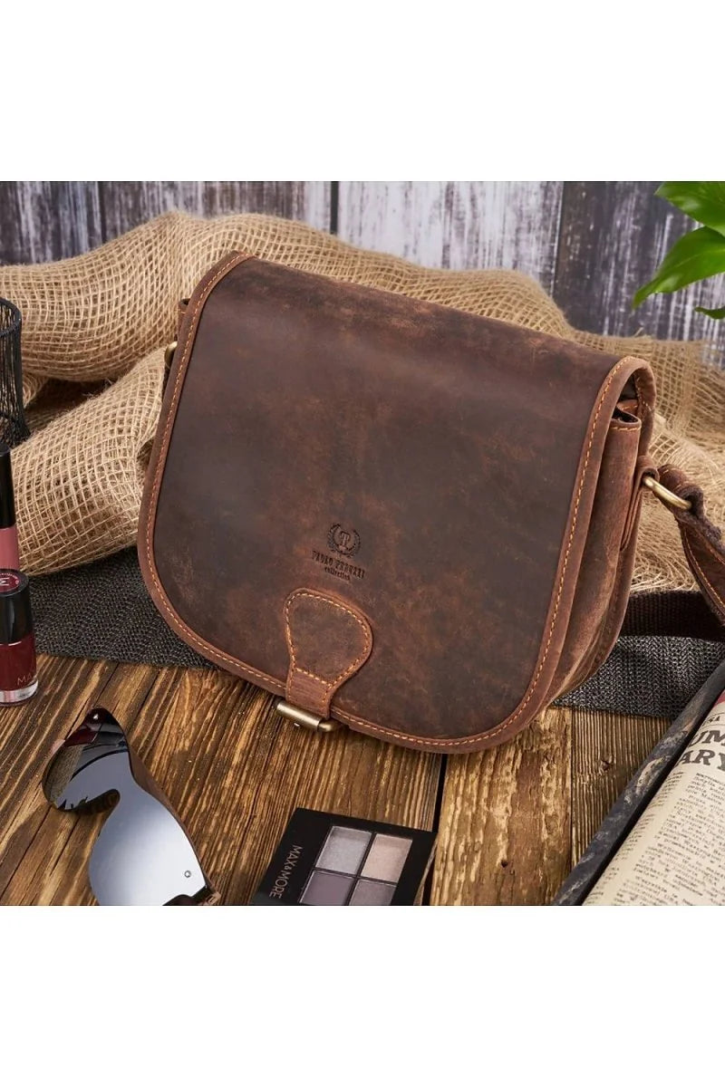 Close-up of a distressed brown leather shoulder bag with a brass buckle closure and stitching detail.