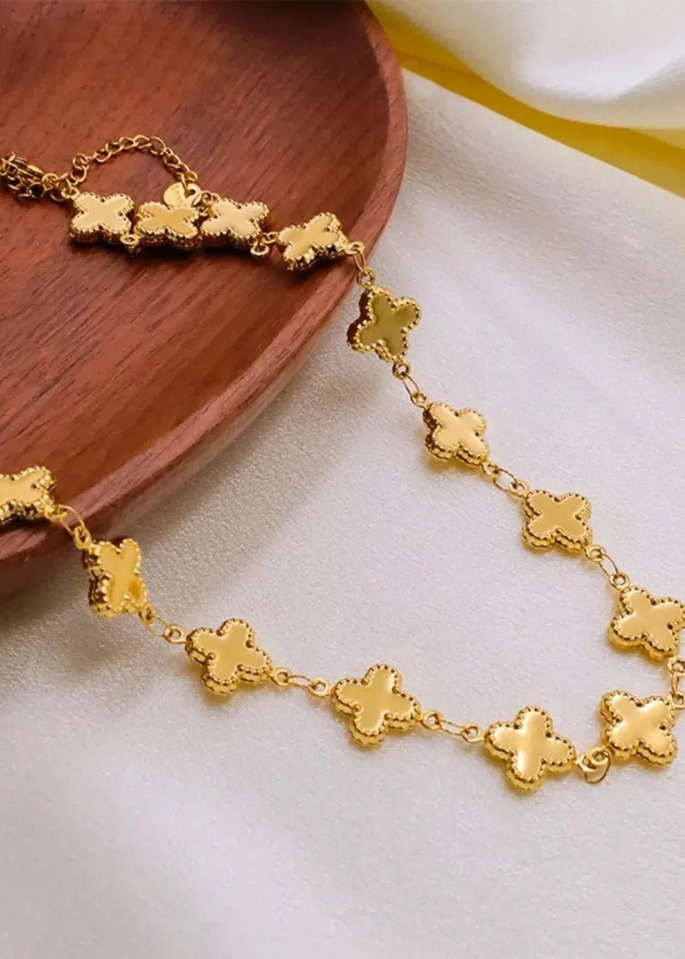 Gold-plated necklace with clover charms on a white satin background.