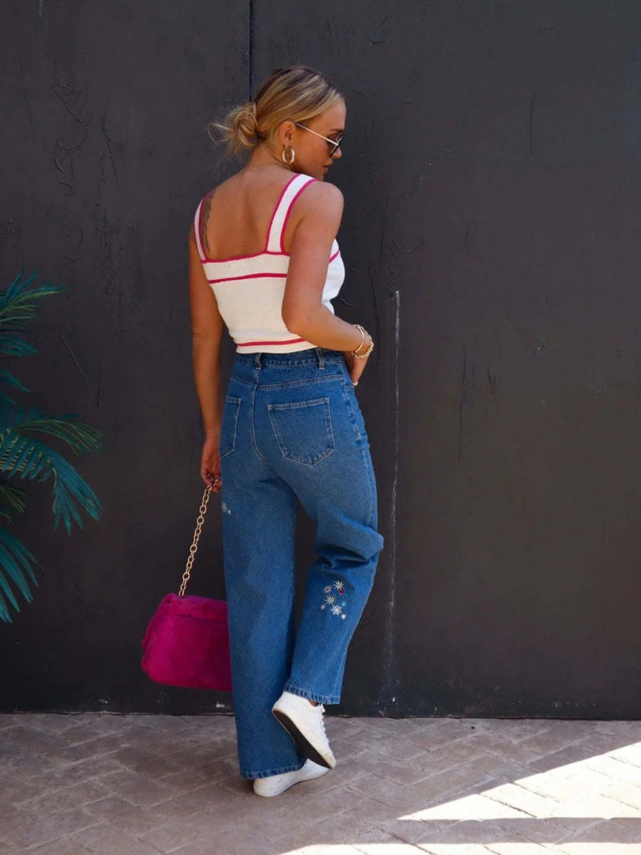Blue denim jeans with embroidered floral details on the leg, worn by a model.