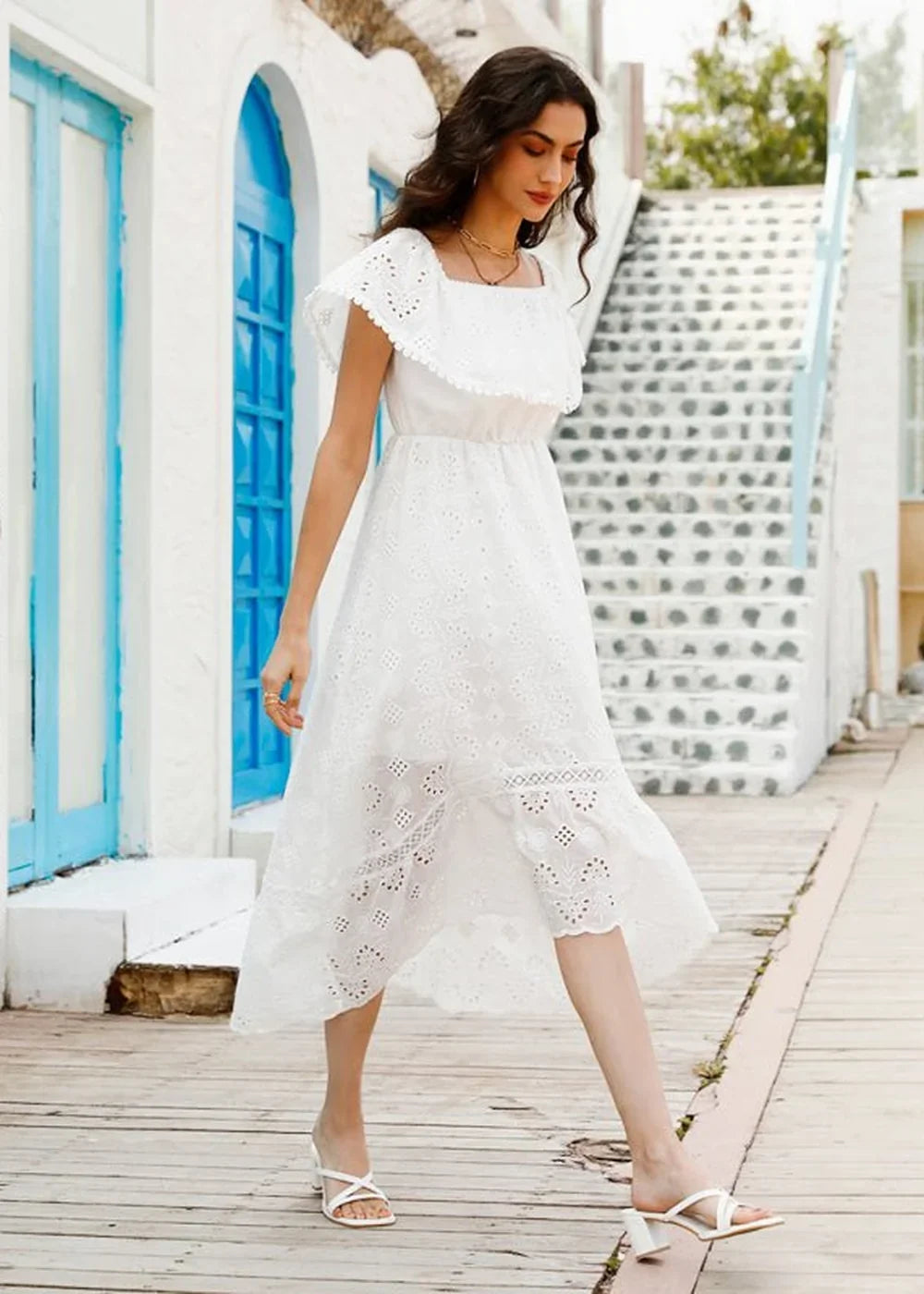Woman in a white cotton eyelet dress with ruffled square neckline and white block heels.