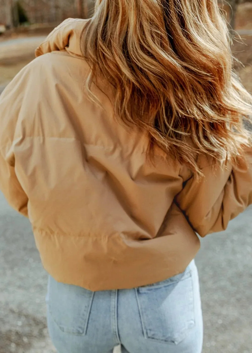 Back view of a woman wearing a tan puffer jacket and light wash jeans.