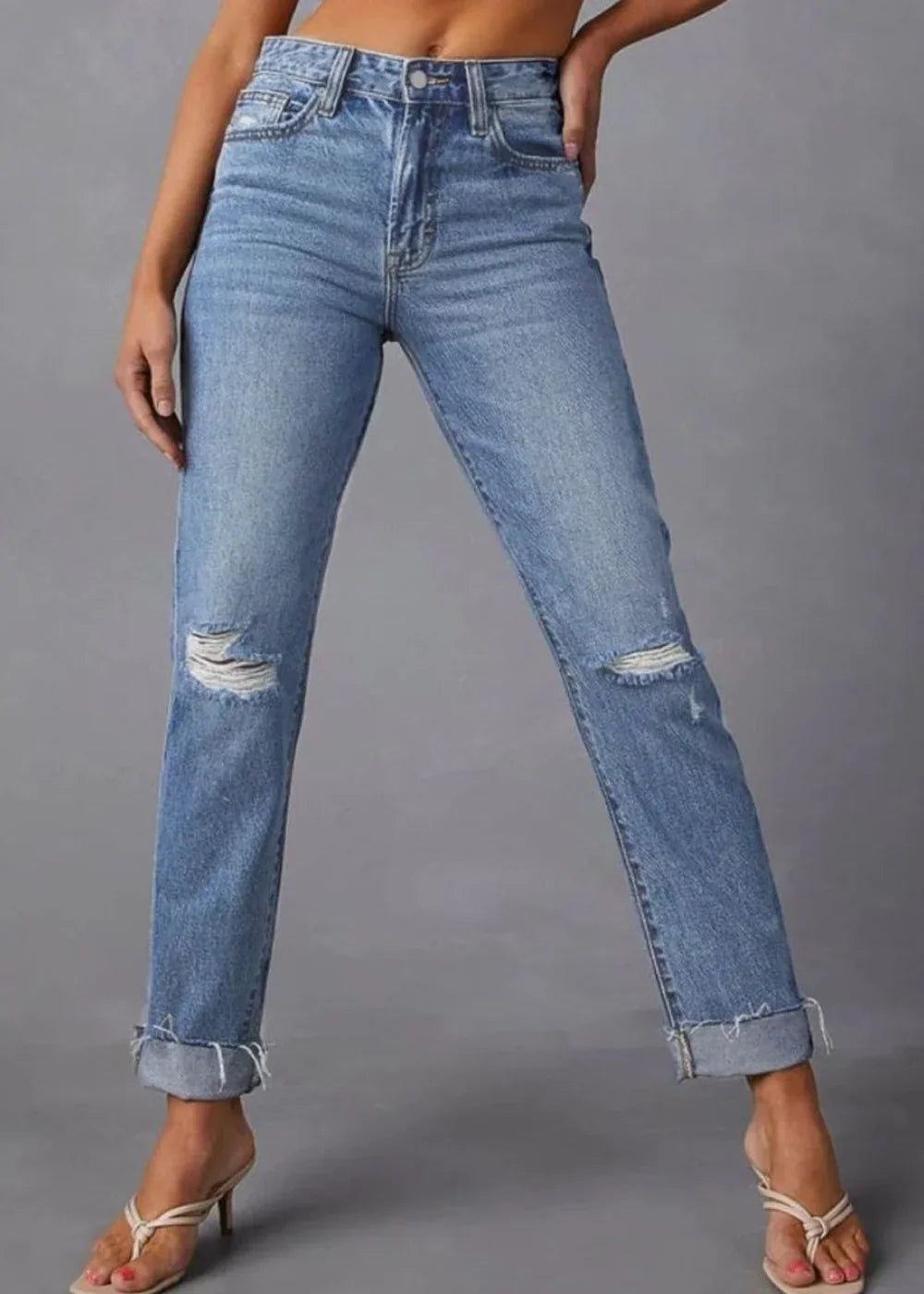 Light wash distressed denim jeans with ripped knees and cuffed hems, on model.