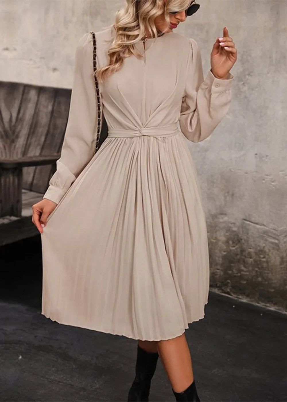 Beige pleated midi dress with a twisted knot detail at the waist and long sleeves, worn by a model.