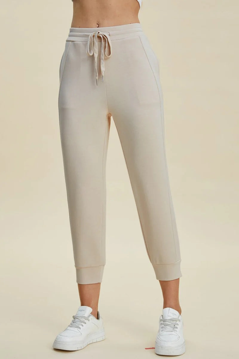 Light beige joggers with a drawstring waist and cuffed ankles, shown on a model.