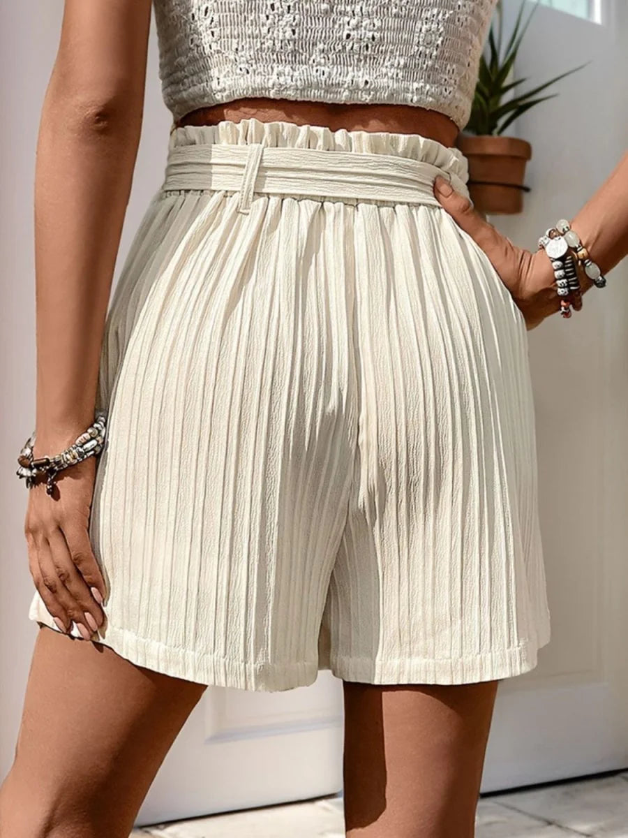 Cream textured shorts with paperbag waist and belt, showing vertical pleats and regular fit.