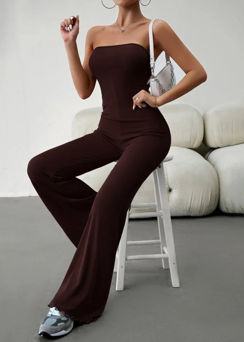 Brown strapless wide-leg jumpsuit with a white crossbody bag and grey sneakers.