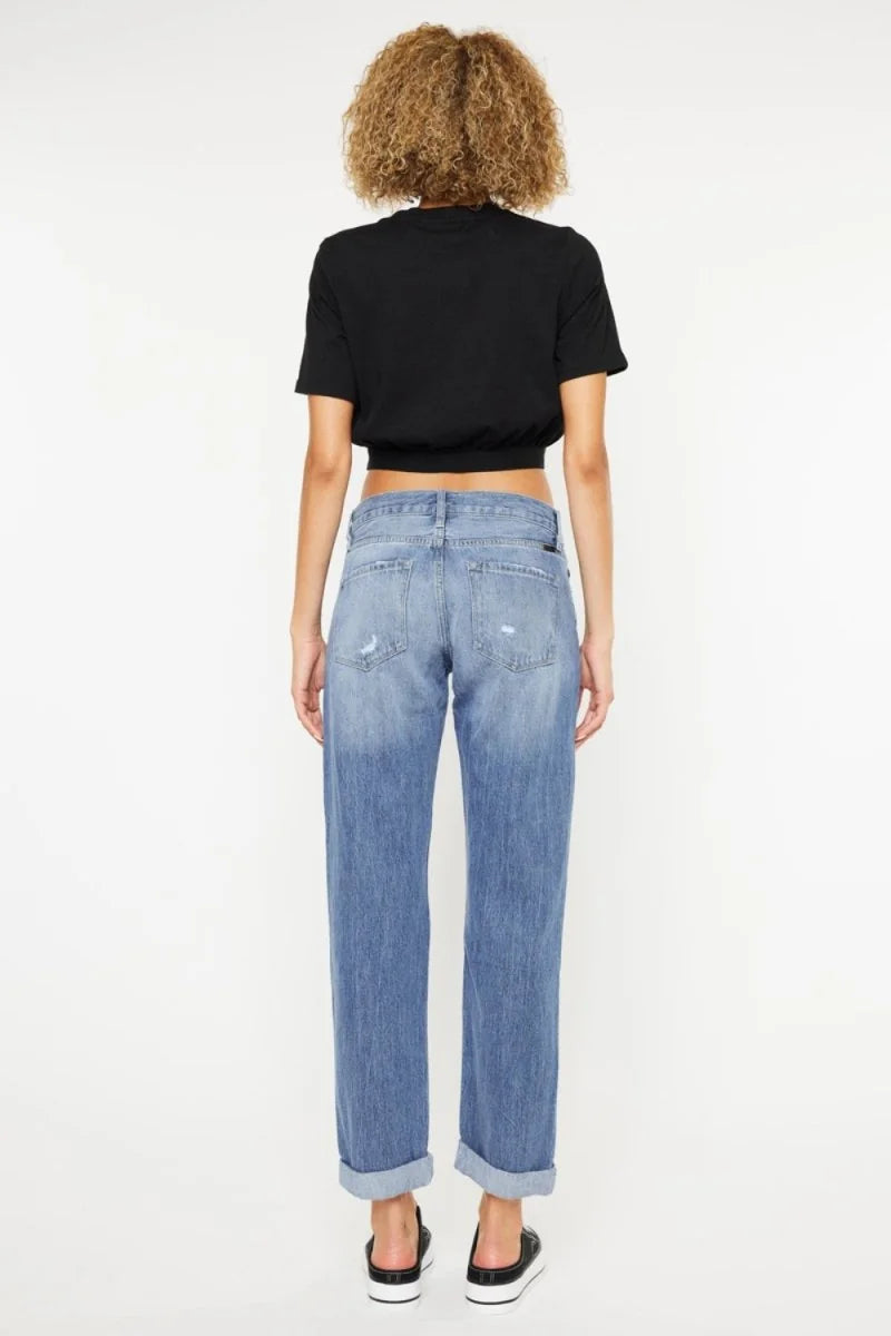 Back view of woman wearing distressed light wash denim jeans with cuffed hems and a black cropped t-shirt.