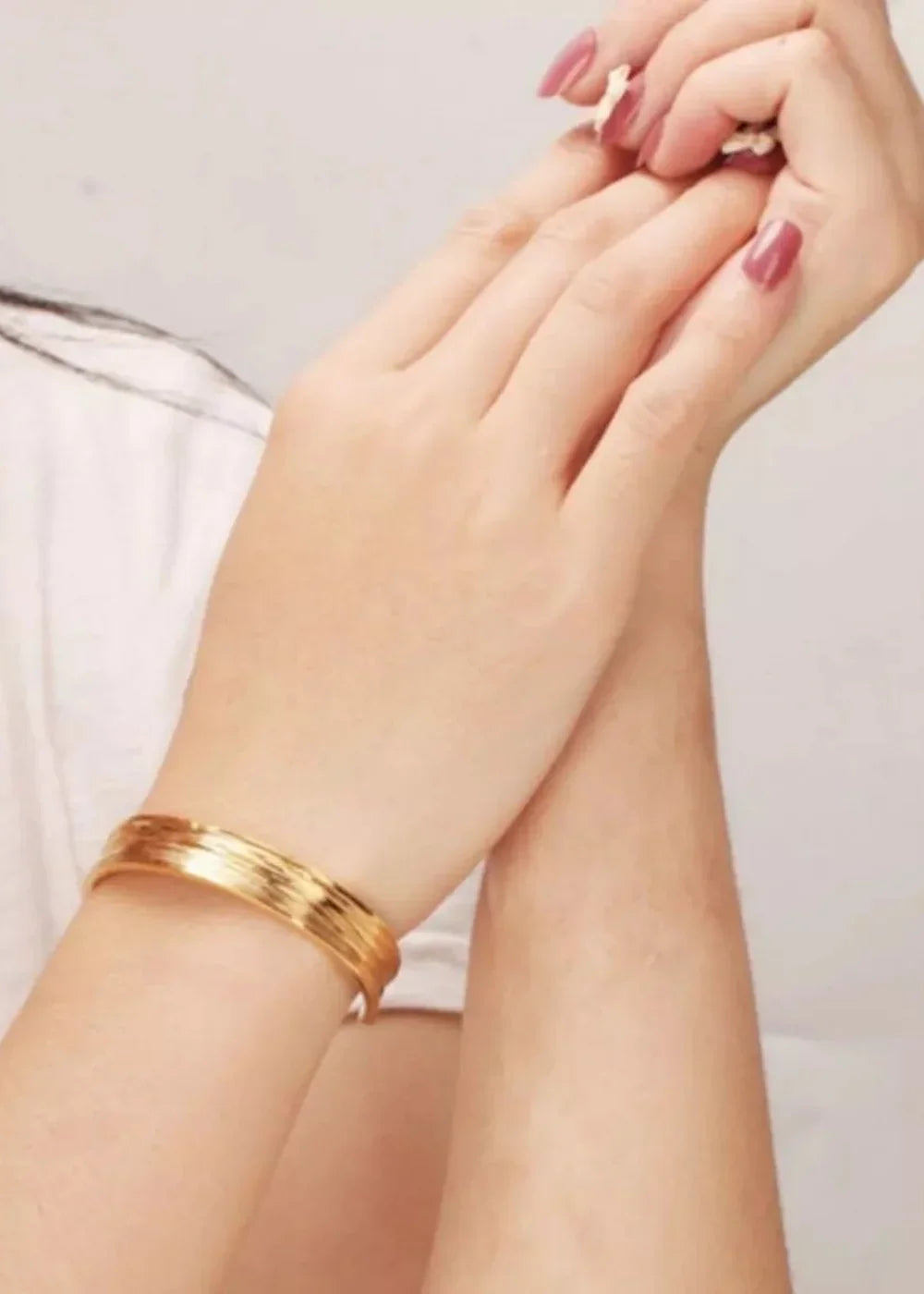 Gold-plated layered cuff bracelet on a woman's wrist, showing a subtle sheen.