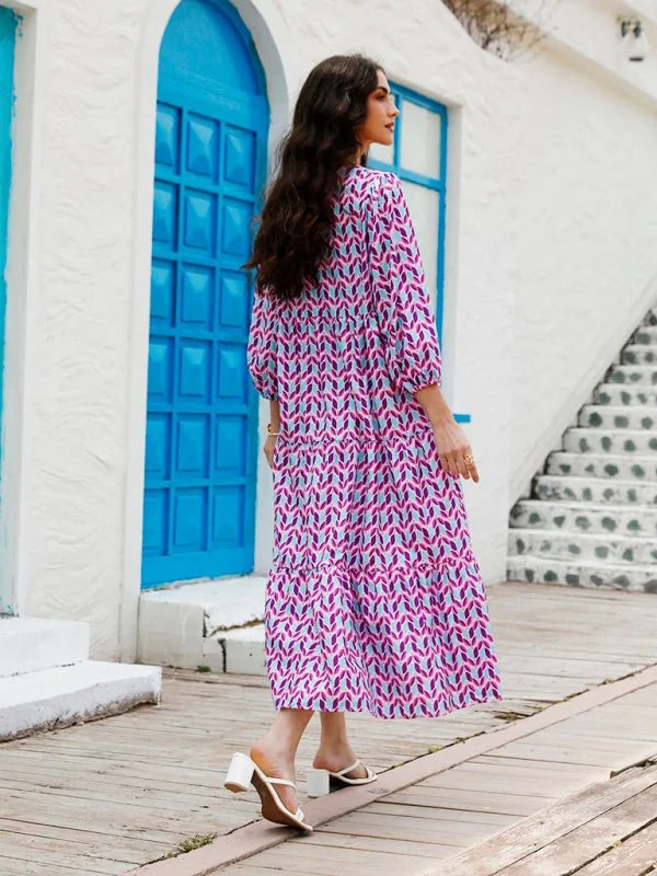 Woman in tiered geometric print midi dress with white block heel mules, walking on wooden planks.