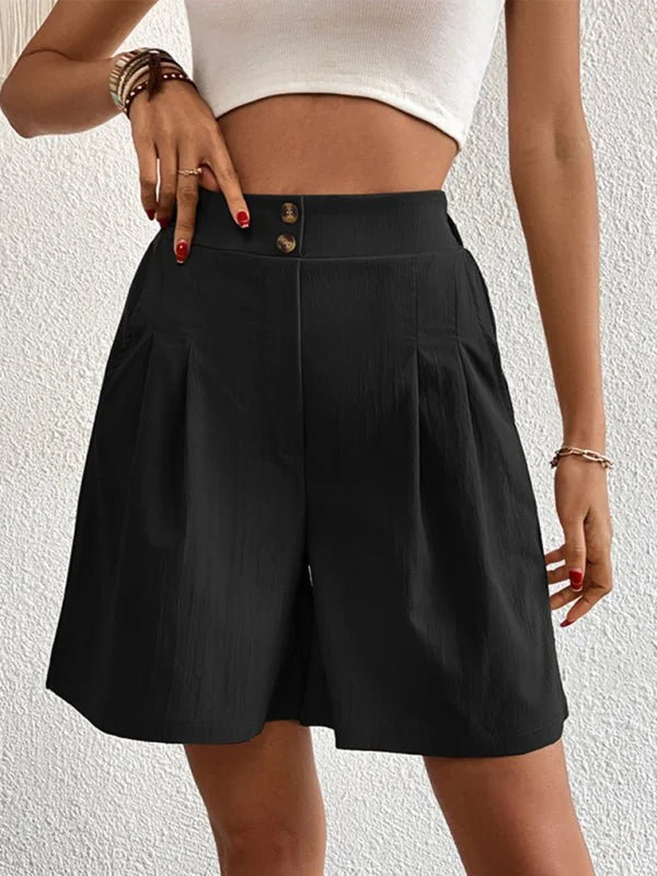 Black high-waisted pleated shorts with button details, on a model.