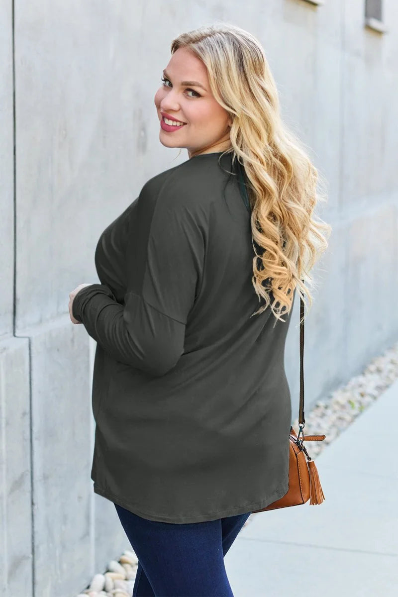 Woman with blonde wavy hair wearing a dark gray long-sleeved top and dark blue jeans, carrying a brown purse.