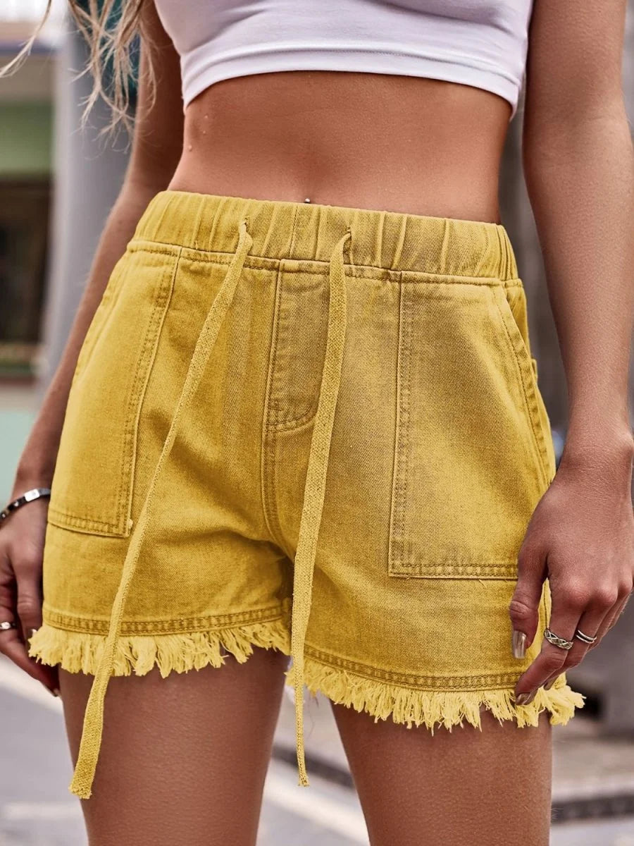 Close-up of yellow denim shorts with frayed hem and drawstring waist on a model.