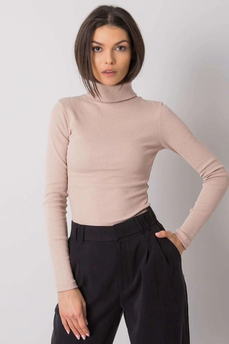 Beige ribbed turtleneck sweater with long sleeves, worn with black wide-leg pants.