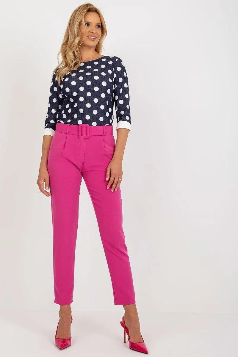 Model in bright pink high-waisted pants with a matching belt and a navy blue polka dot blouse.
