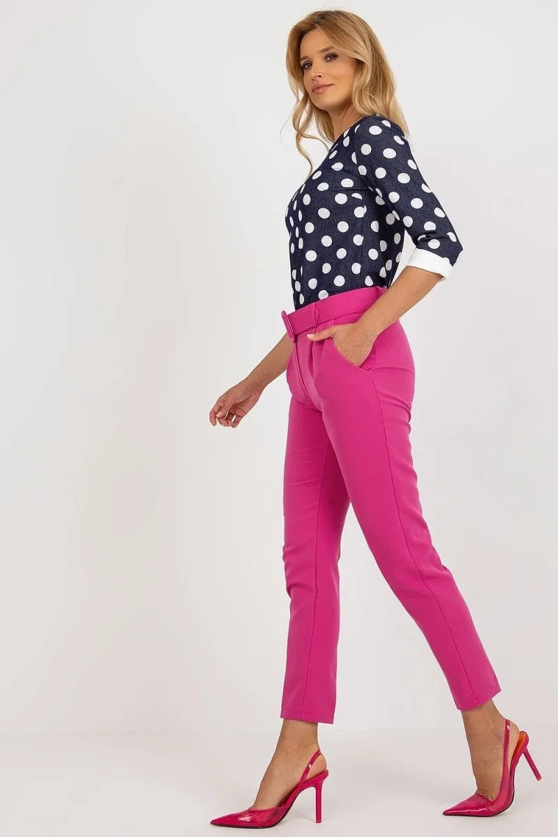 Model wearing bright pink, high-waisted pants with a belted waist and pointed-toe heels.