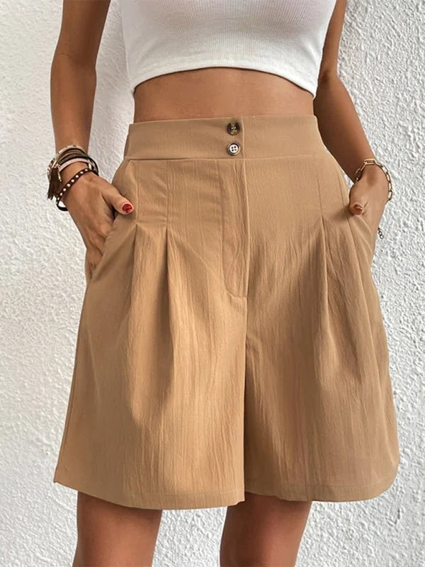 Tan pleated shorts with a high waist and button closure, on a woman.