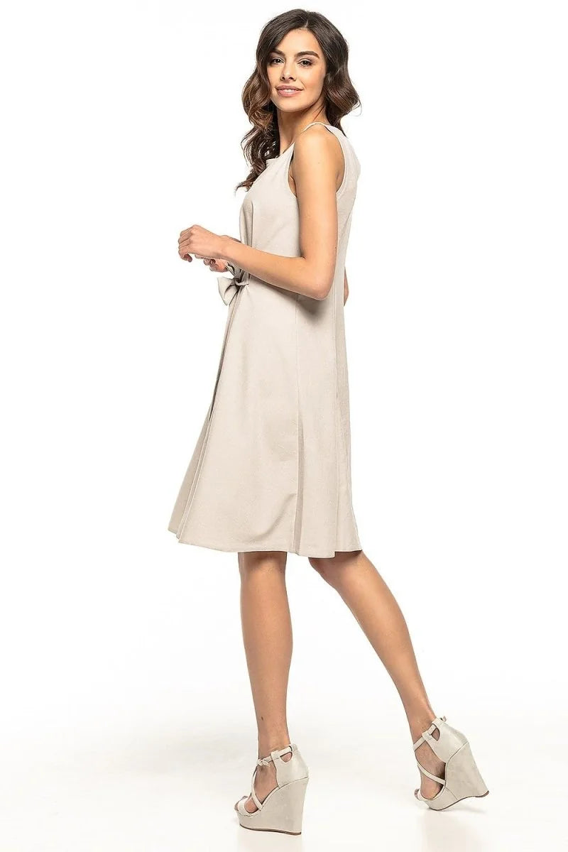 Light beige sleeveless dress with a belted waist, showing pleats and wedge sandals.