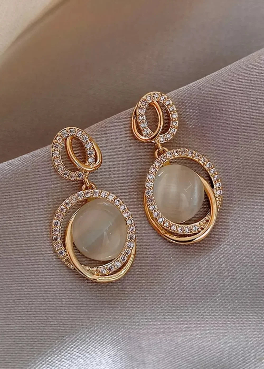 Gold-plated earrings with rhinestones and a creamy cat's eye stone, elegantly displayed.