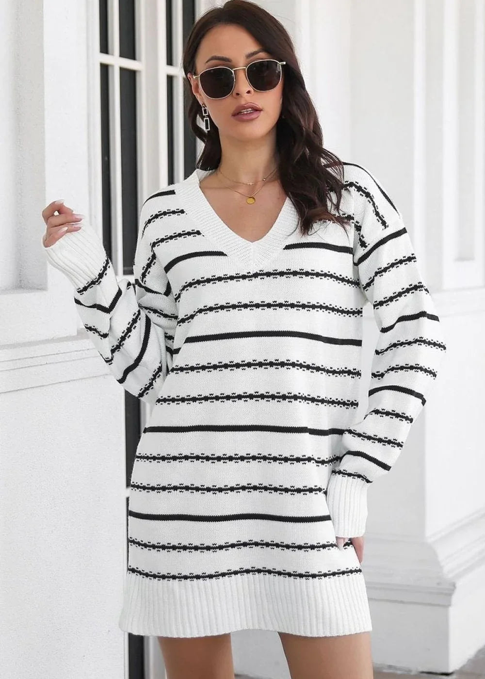 A woman wears a white sweater dress with black horizontal stripes and a v-neck.