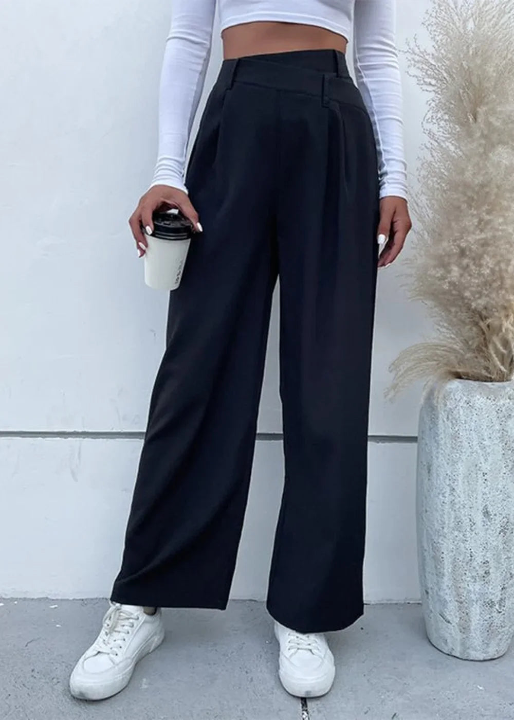 Black wide-leg trousers with a high waist and pleats, paired with white sneakers.