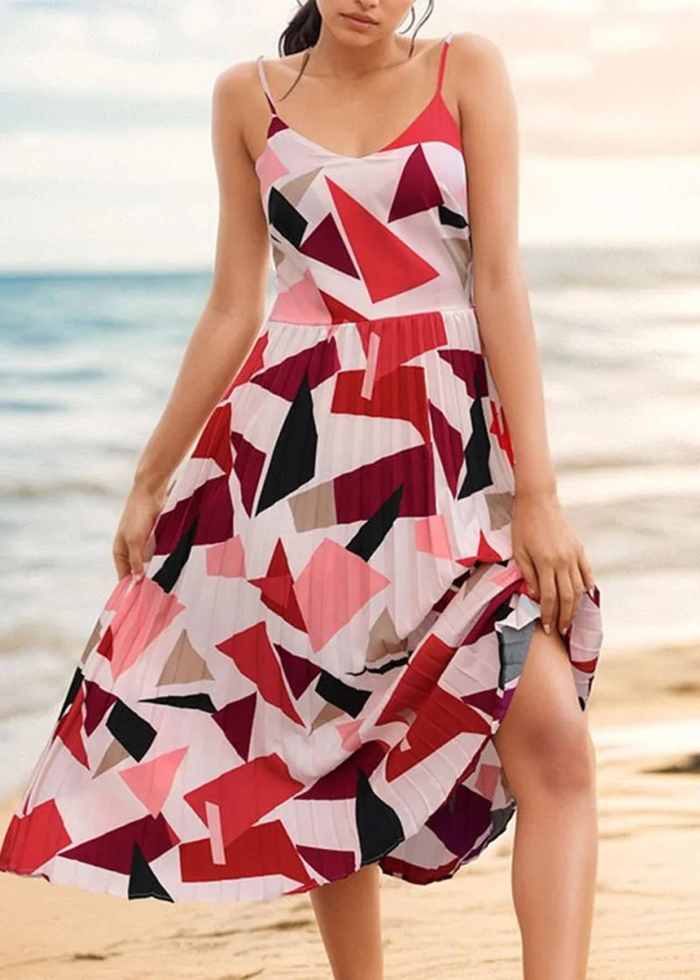 A woman models a white midi dress with a bold geometric print in red, pink, and black, featuring a pleated skirt and spagh...