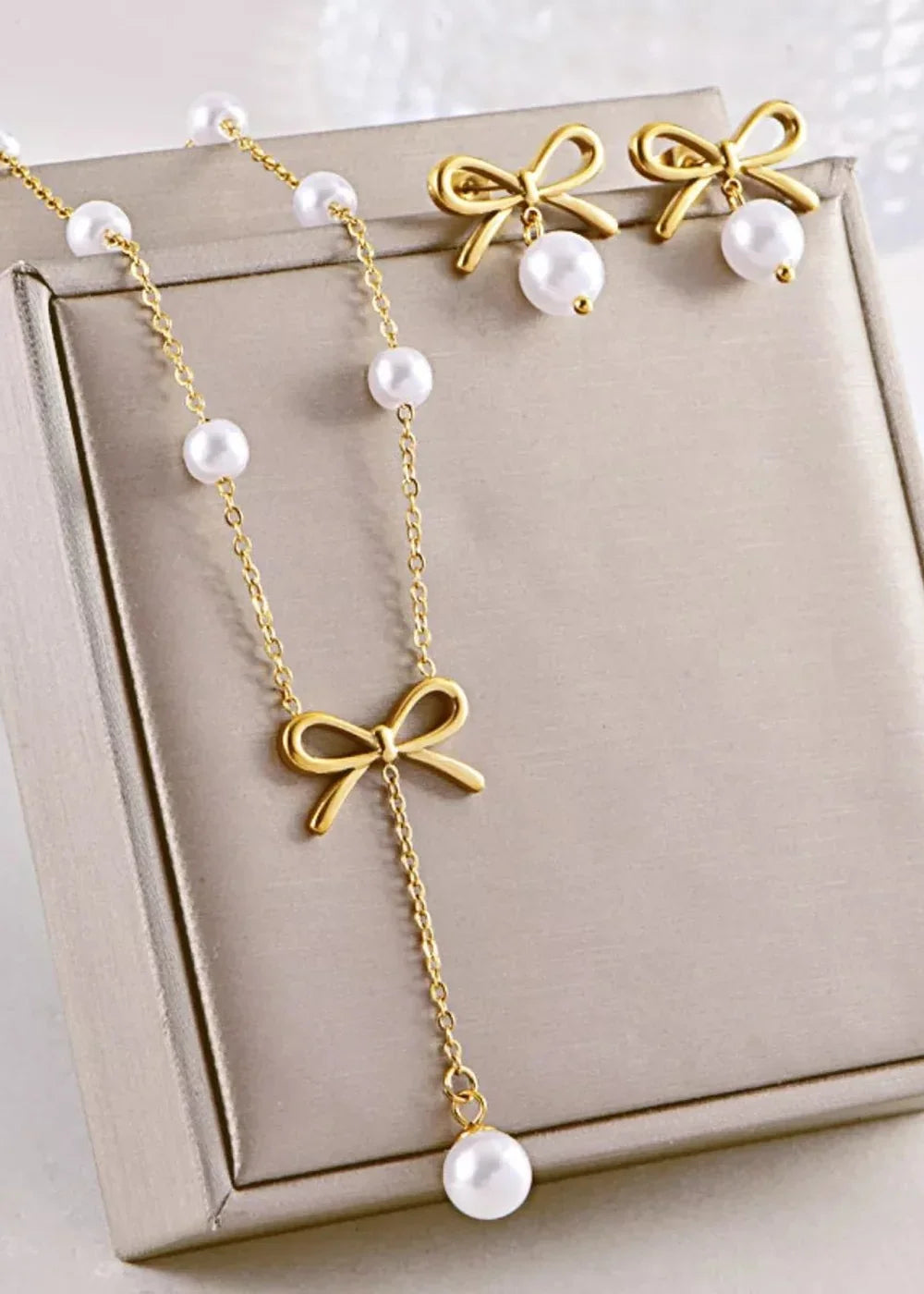 Gold necklace with pearls and a bow pendant, and matching bow earrings with pearl drops.