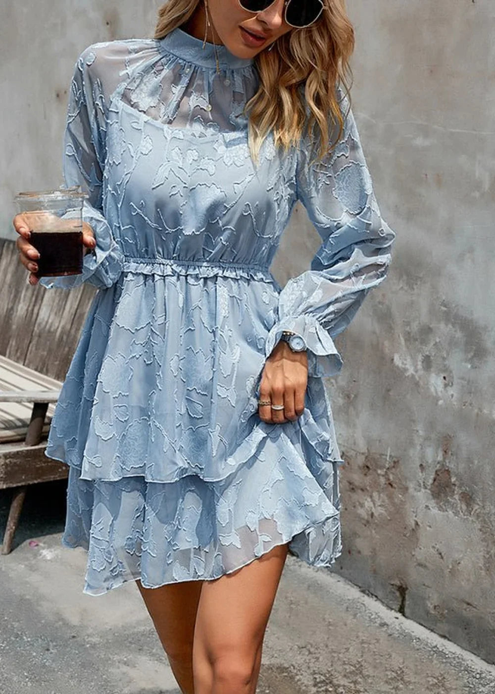 Light blue tiered lace dress with ruffled neckline and cinched waist, held by a woman with a drink.