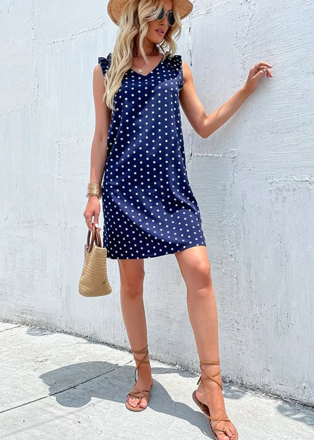 Navy blue polka dot sleeveless dress with ruffled shoulders and straw bag.