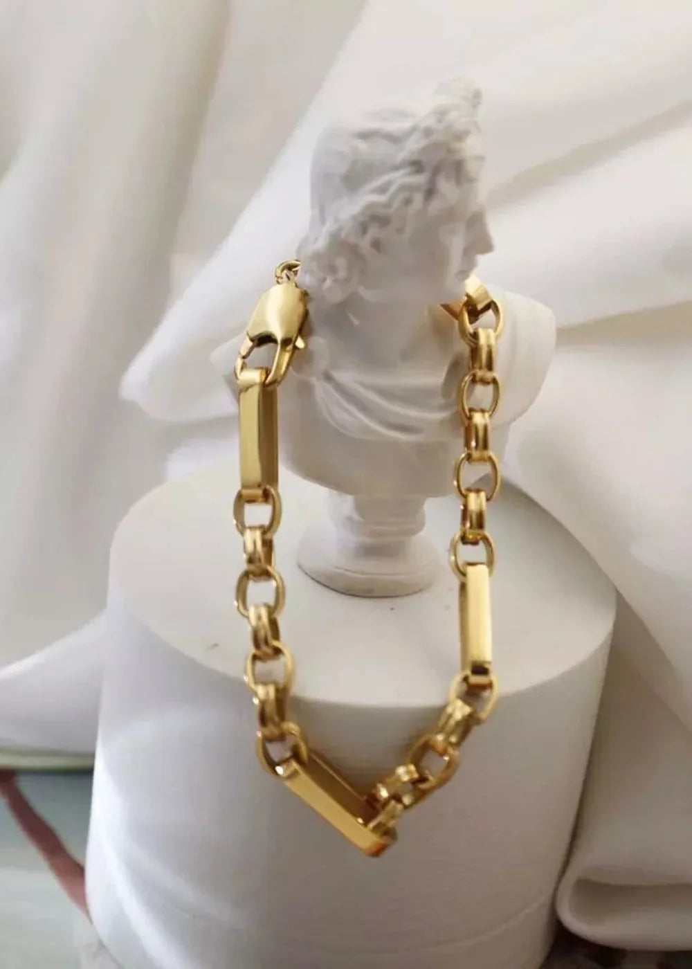 Gold chain bracelet with rectangular links and circular links, displayed on a white bust.