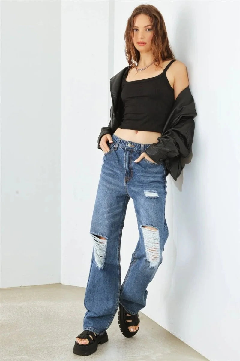 Distressed, wide-leg, blue denim jeans on a model, featuring ripped knees and a relaxed fit.