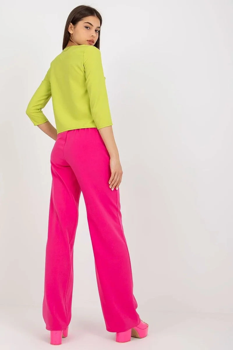 A young woman from behind wears a neon green long-sleeved top and bright pink wide-leg pants with platform heels.