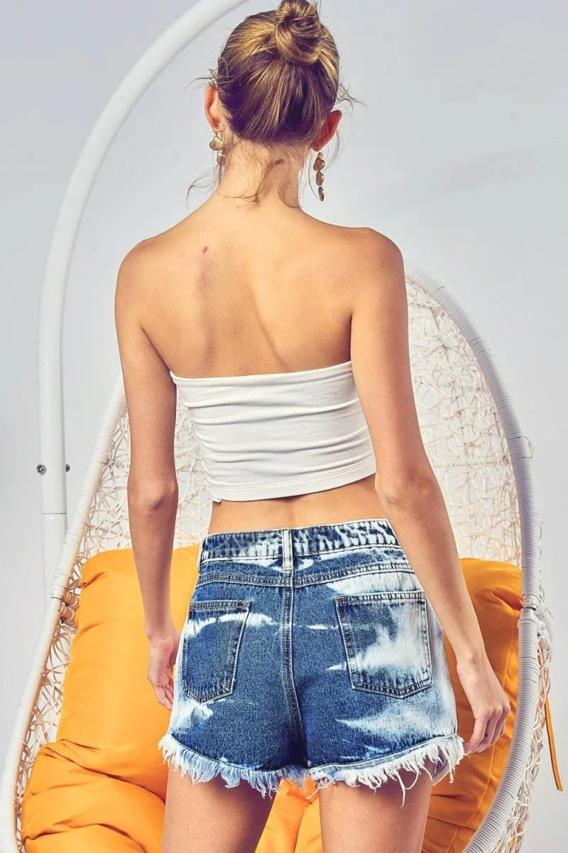 Distressed denim shorts with frayed hem and bleached tie-dye effect, shown from the back on a model.