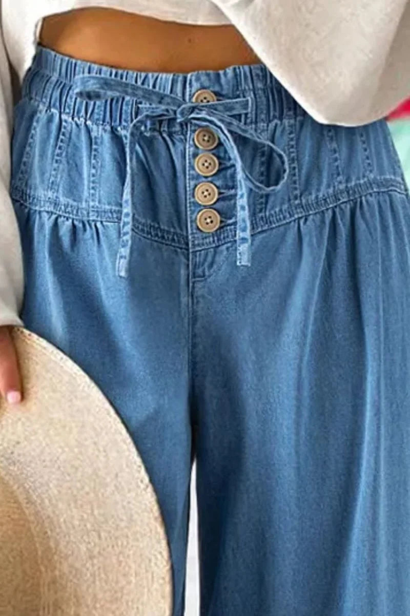Close-up of light blue denim pants with elastic waistband, drawstring, and five decorative buttons.