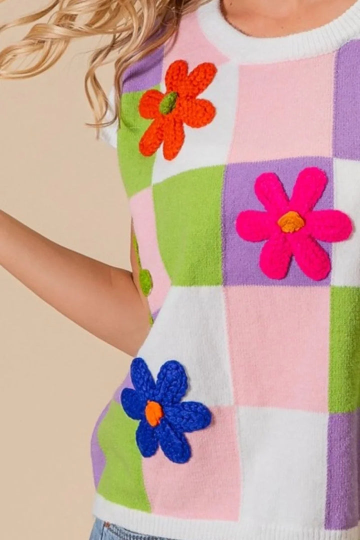Crocheted flower appliqué on a pastel checkered knit vest.