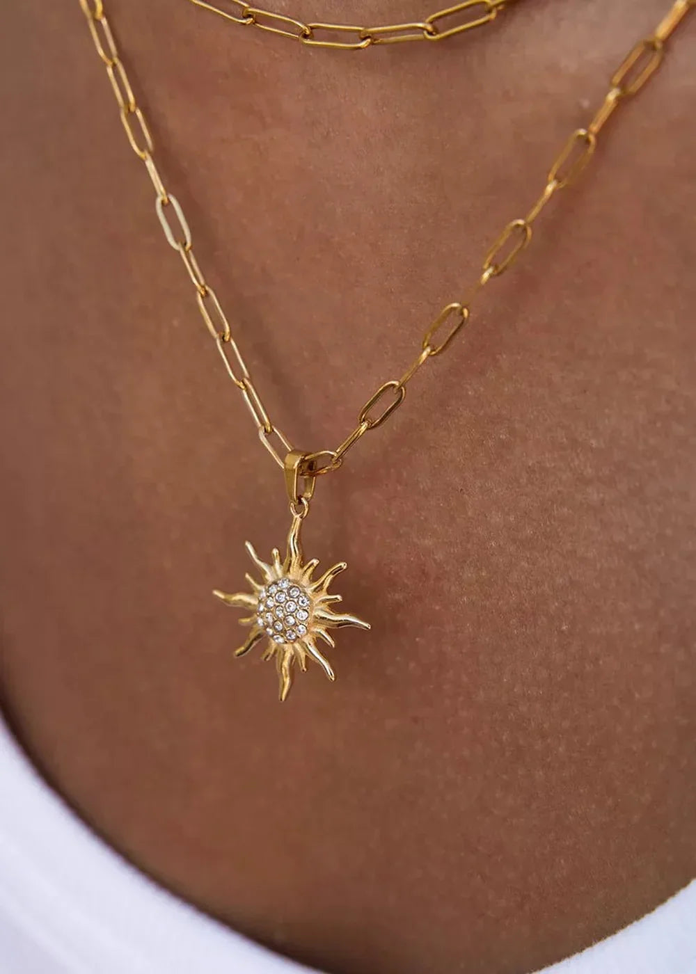 Close-up of a gold chain necklace with a sun pendant encrusted with rhinestones.