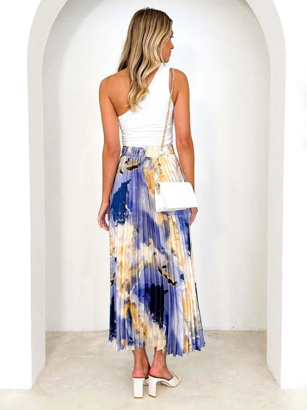 Pleated maxi skirt with abstract blue, white, and gold print, shown on model.