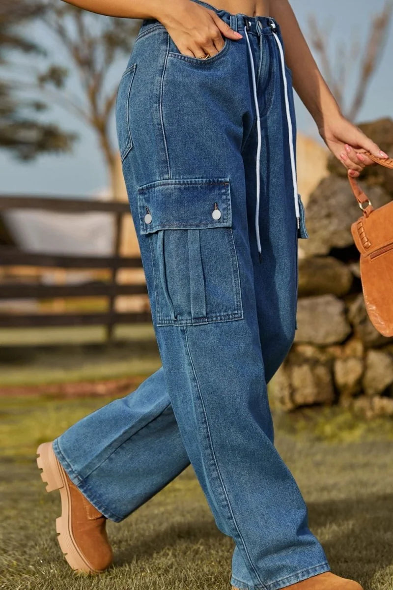 Blue denim cargo pants with pleats and white drawstring, worn by a model with brown boots.